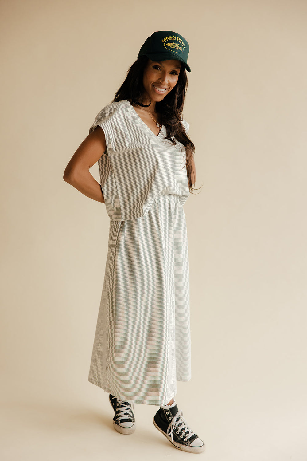 Woman wearing a white dress, green cap, and black sneakers on a beige background