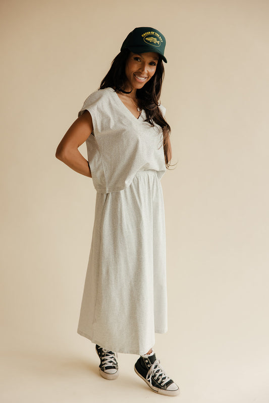 Woman wearing a white dress, green cap, and black sneakers on a beige background