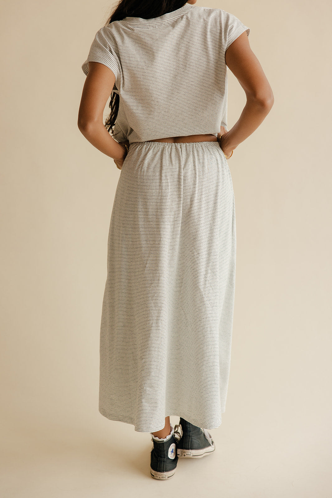 Person wearing a matching top and skirt set with black sneakers on a beige background