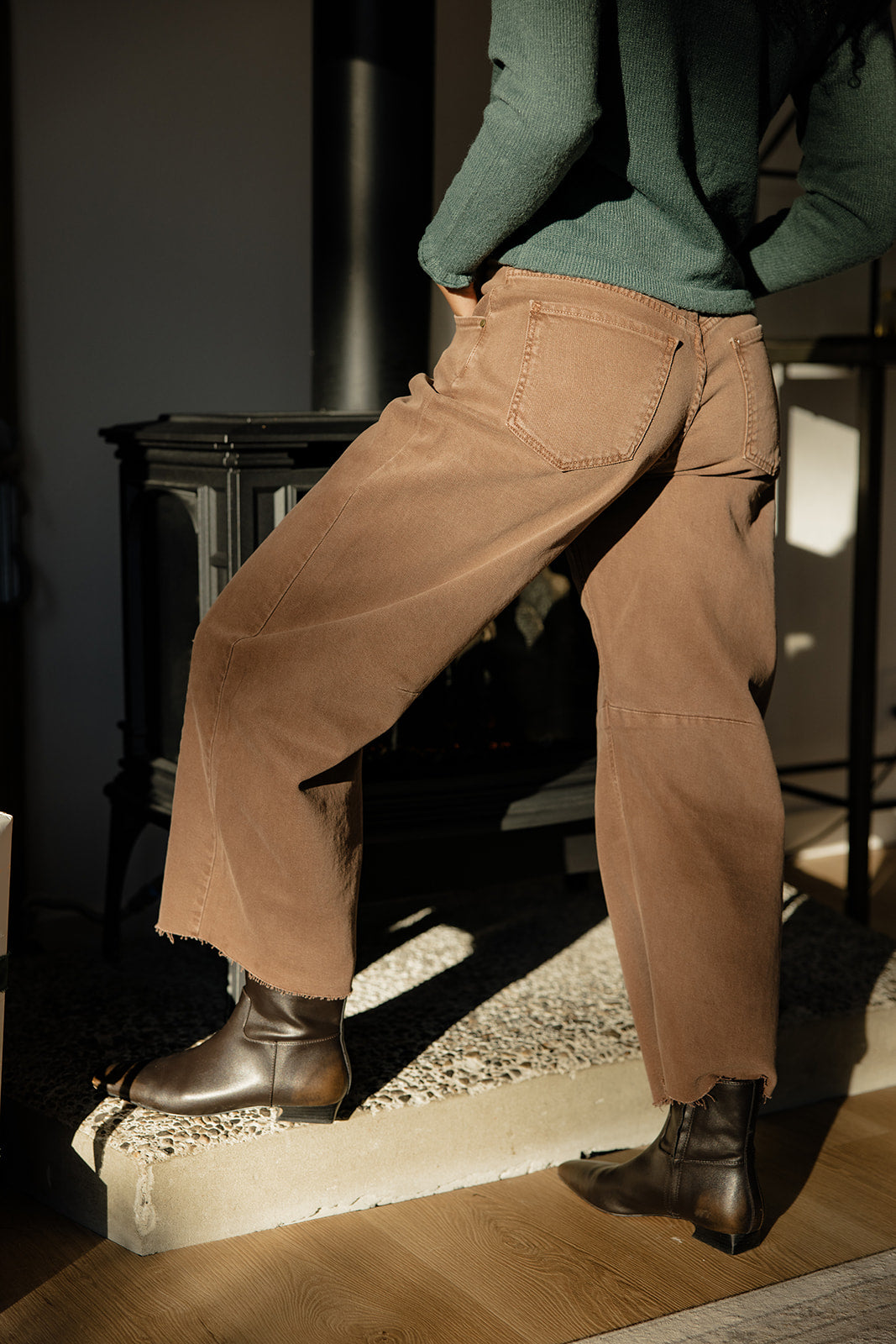 Person wearing brown pants and green sweater standing on a step indoors.