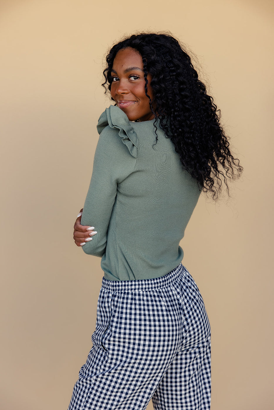 a woman with long curly hair wearing a green shirt and black and white checkered shorts