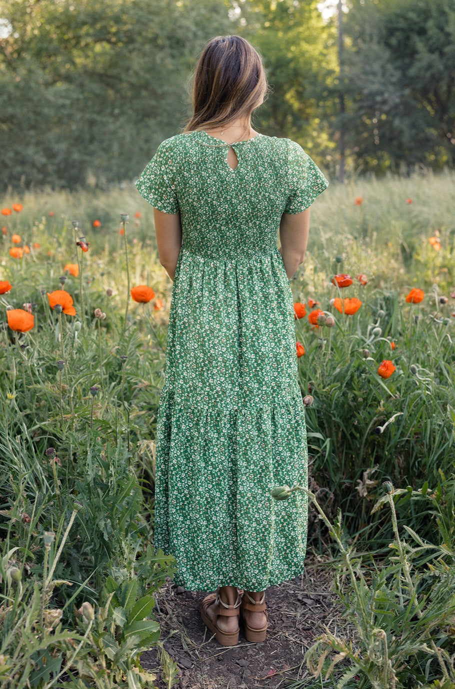 a woman in a green dress standing in a field of flowers