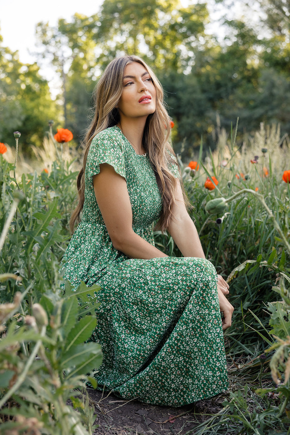 a woman in a green dress sitting in a field of flowers