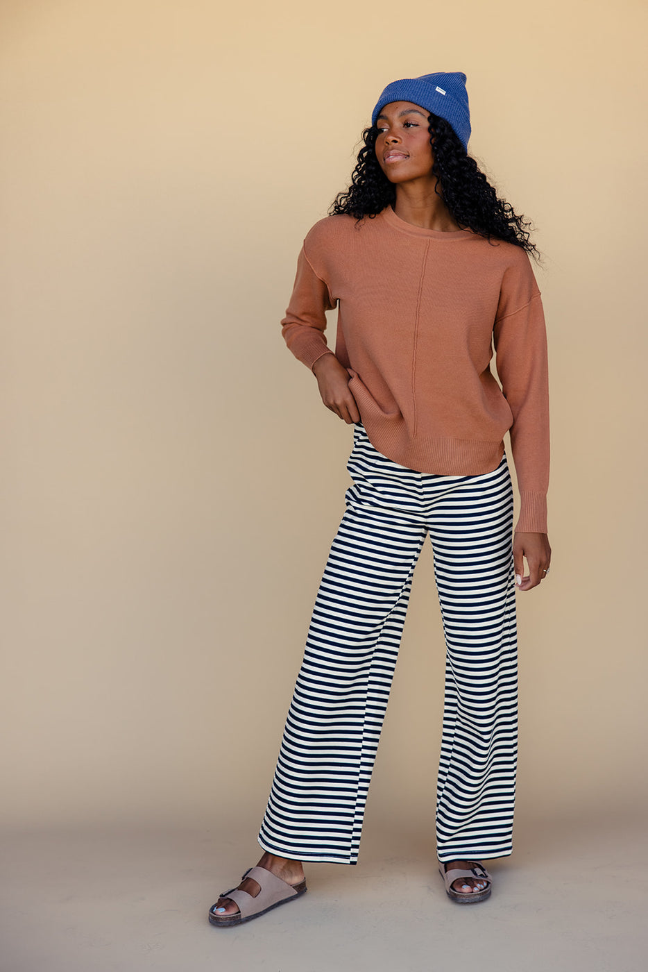 a woman in a brown sweater and striped pants