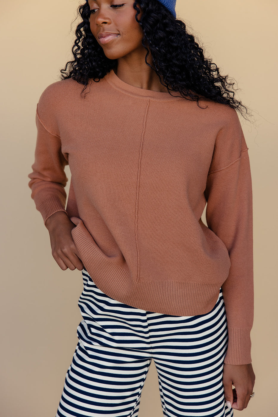 a woman wearing a brown sweater and striped pants