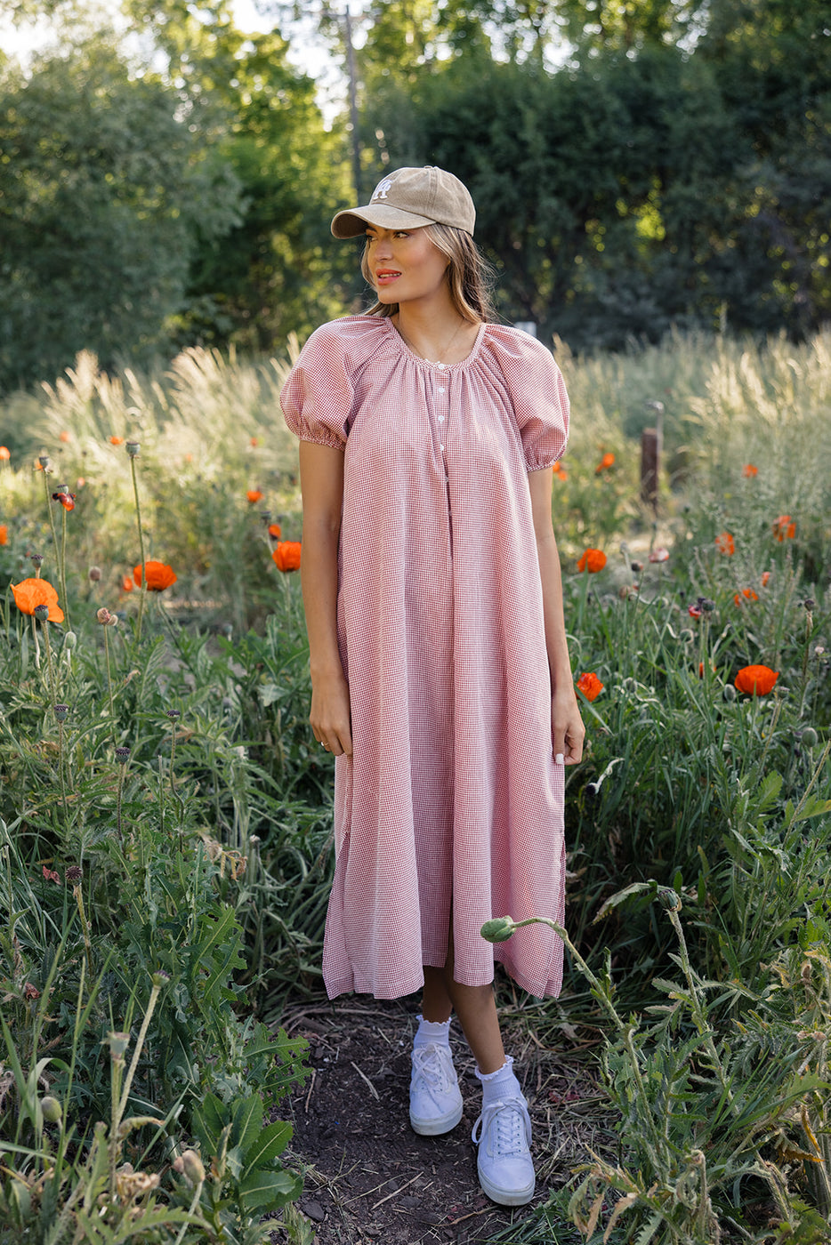 a woman in a hat standing in a field of flowers