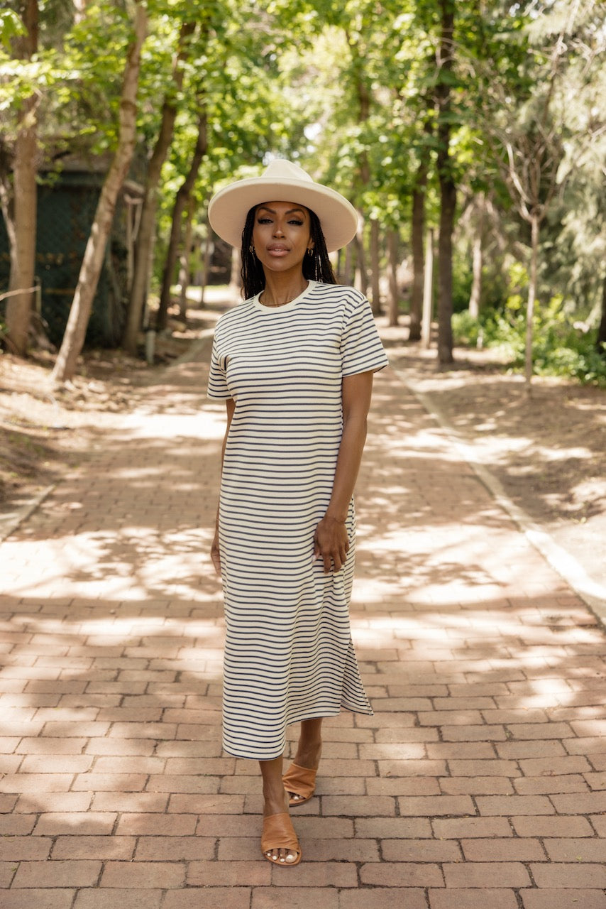 a woman in a long striped dress and hat standing on a brick path