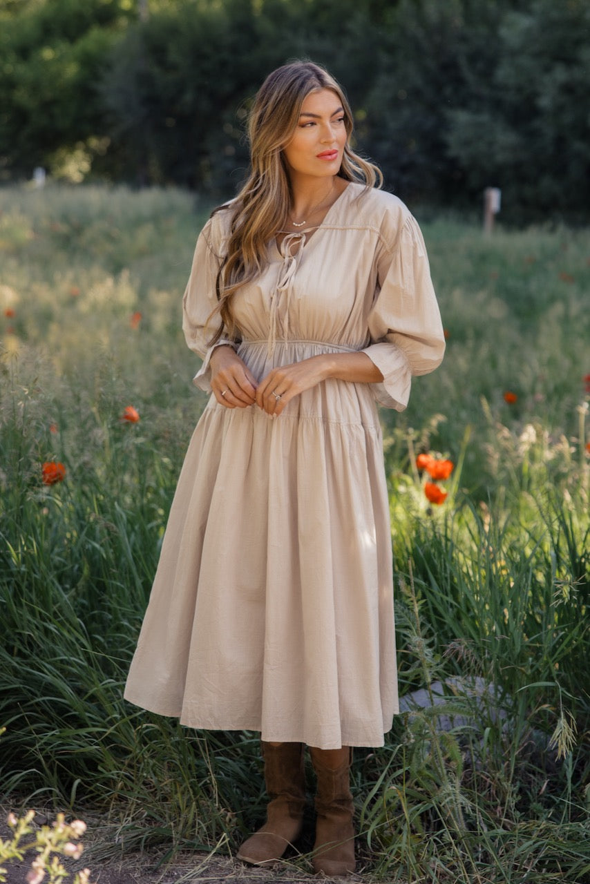 a woman in a dress standing in a field of tall grass