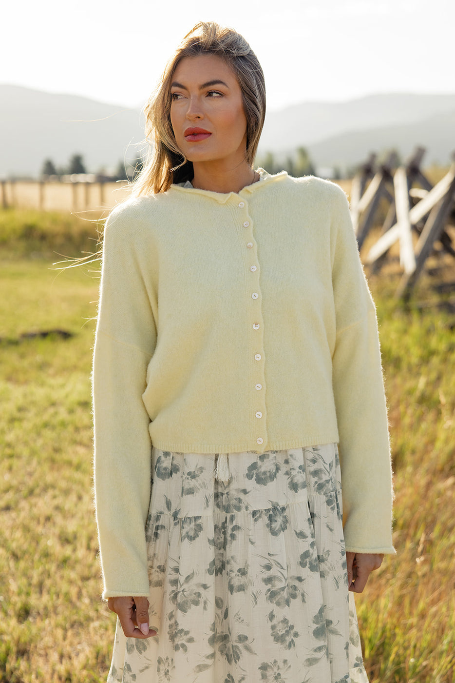 a woman in a white sweater and skirt standing in a field