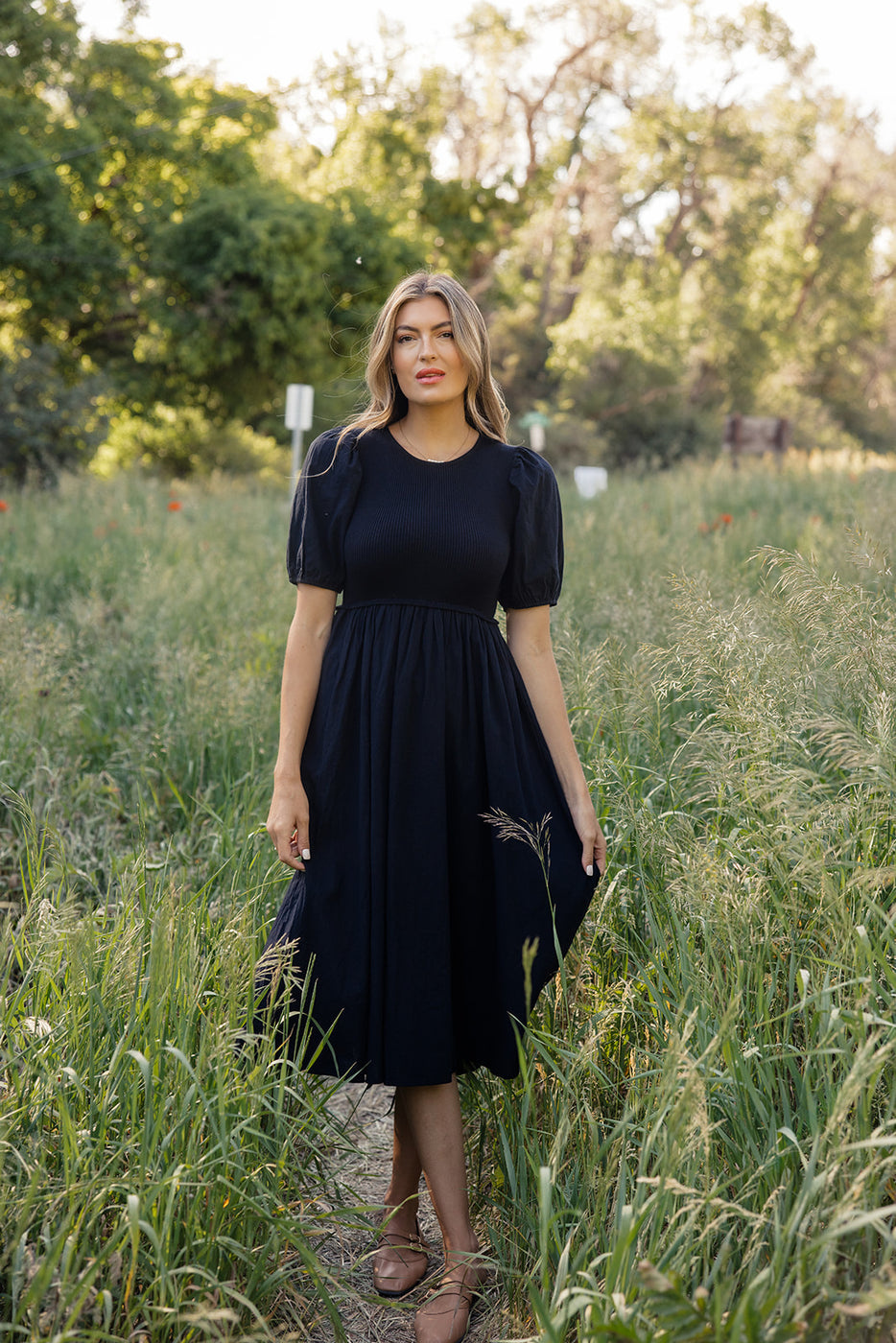 a woman in a black dress standing in tall grass