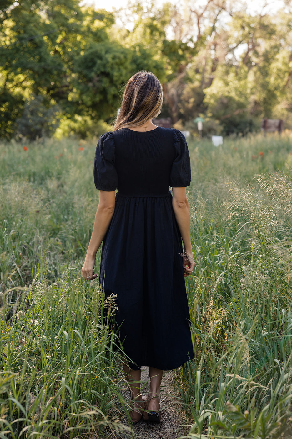 a woman in a black dress standing in tall grass