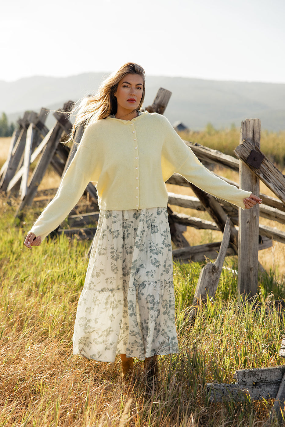 a woman in a long white dress and a white sweater standing in a field