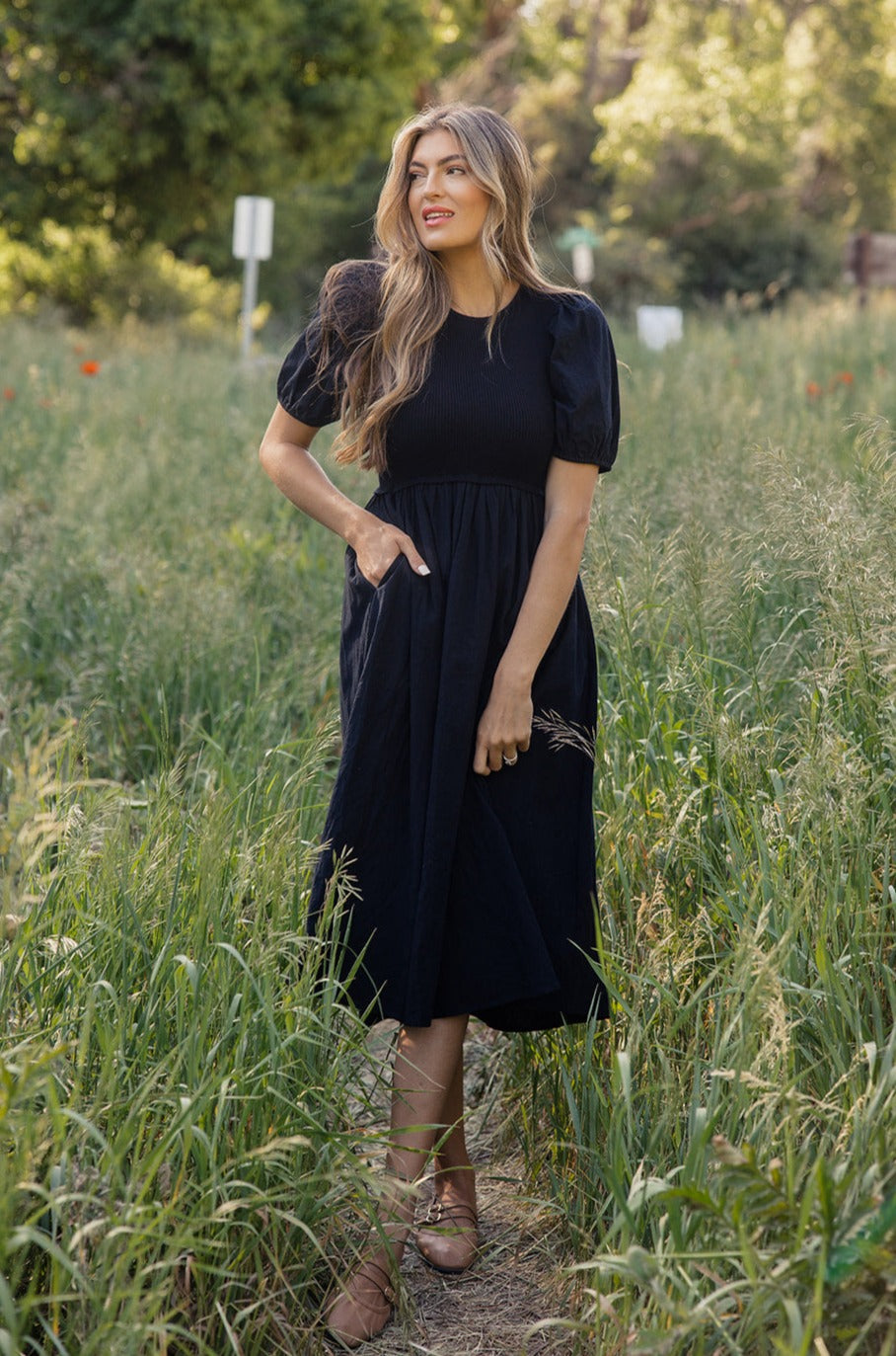 a woman in a black dress standing in tall grass