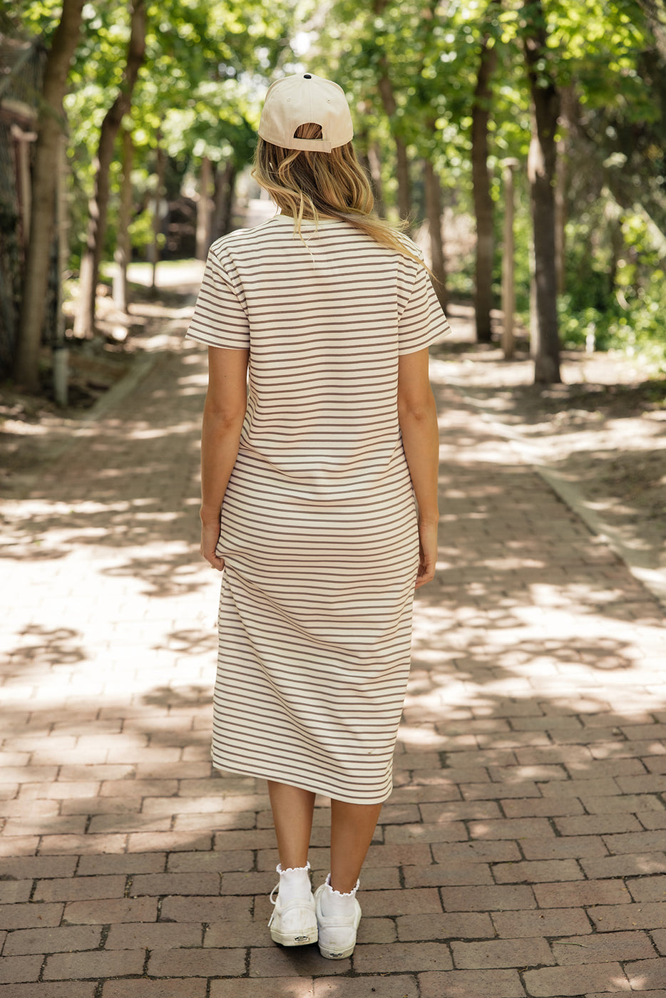 a woman in a striped dress walking on a brick path