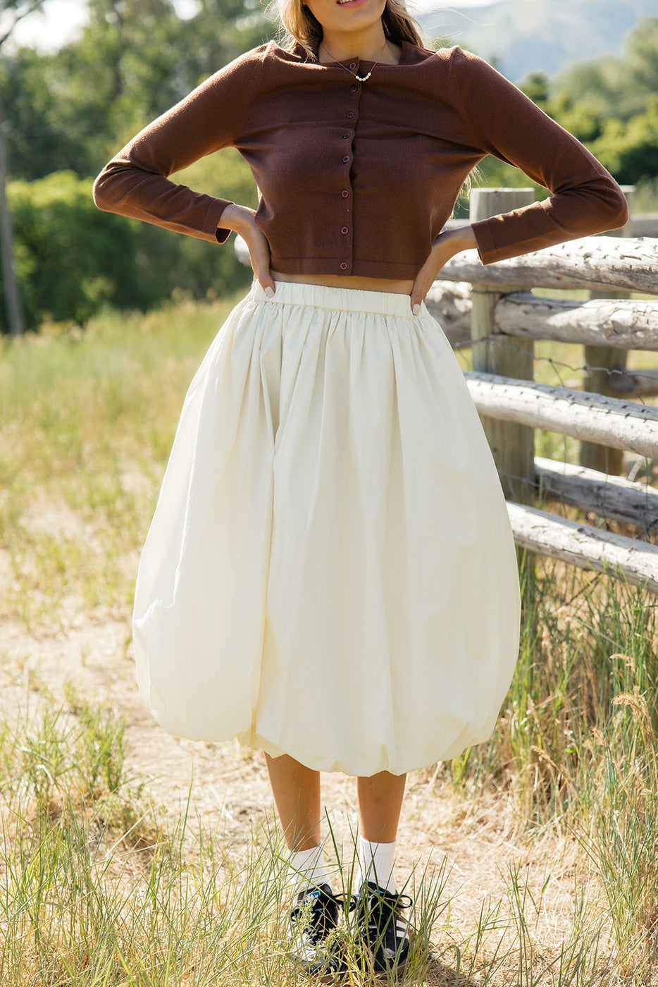 a woman in a white skirt and a brown sweater