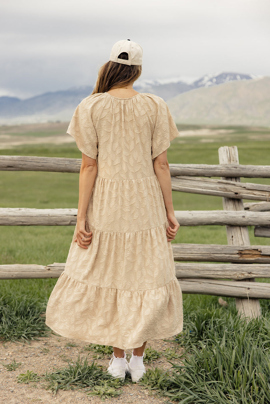 a woman in a long dress standing by a fence