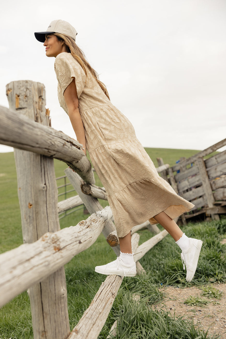 a woman in a dress and white shoes standing on a wooden fence