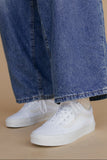 Person wearing blue jeans and white sneakers on a beige background