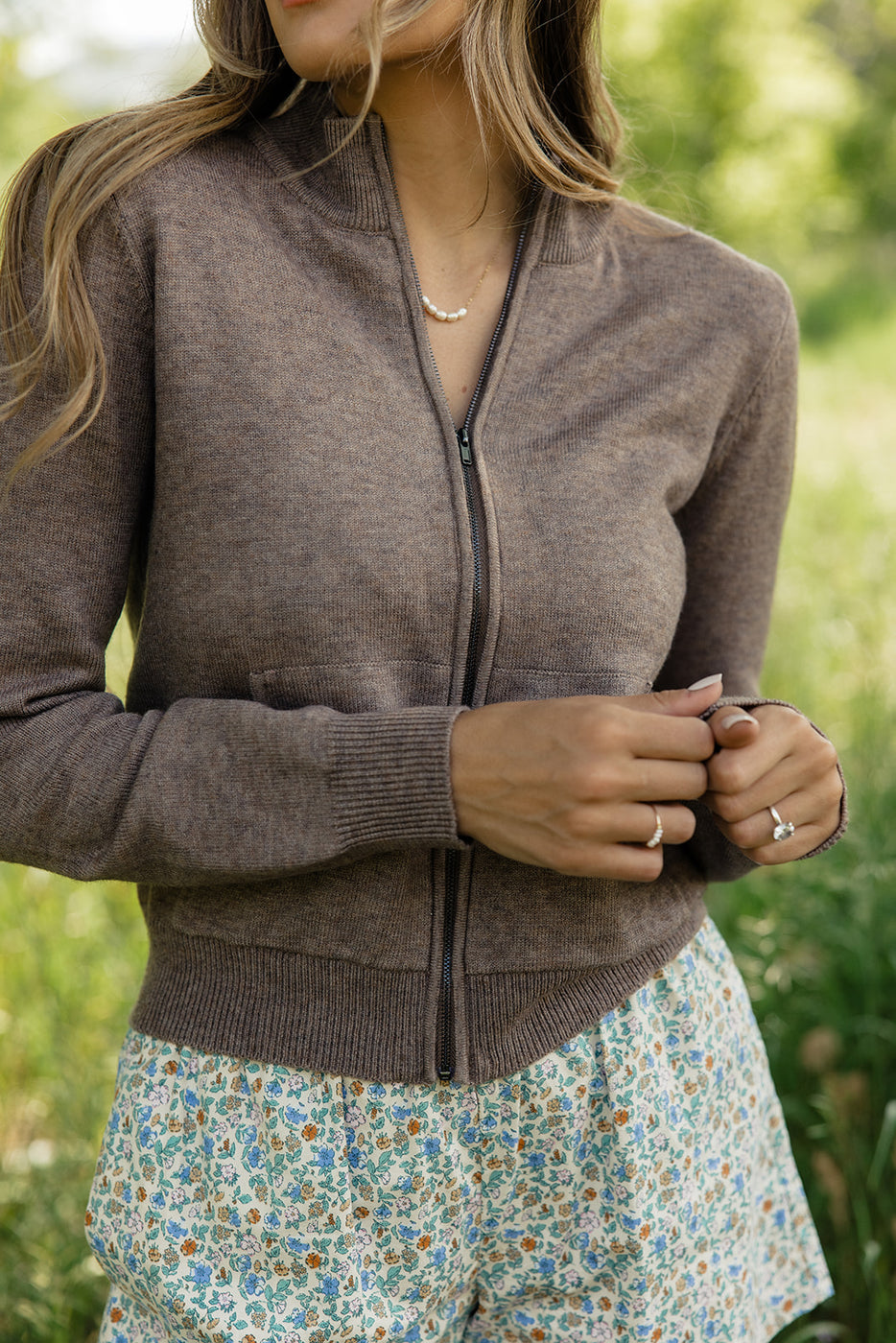 a woman wearing a brown sweater and floral skirt