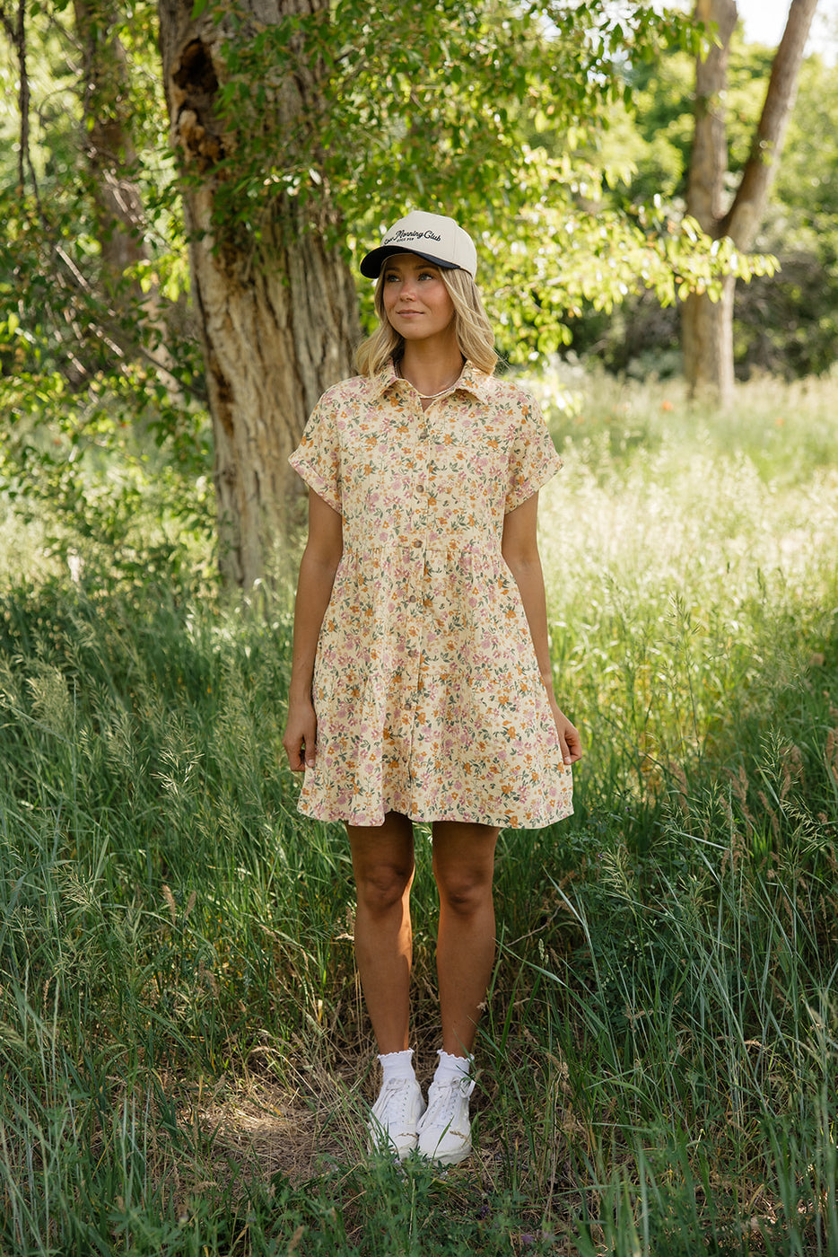 a woman in a dress and hat standing in grass