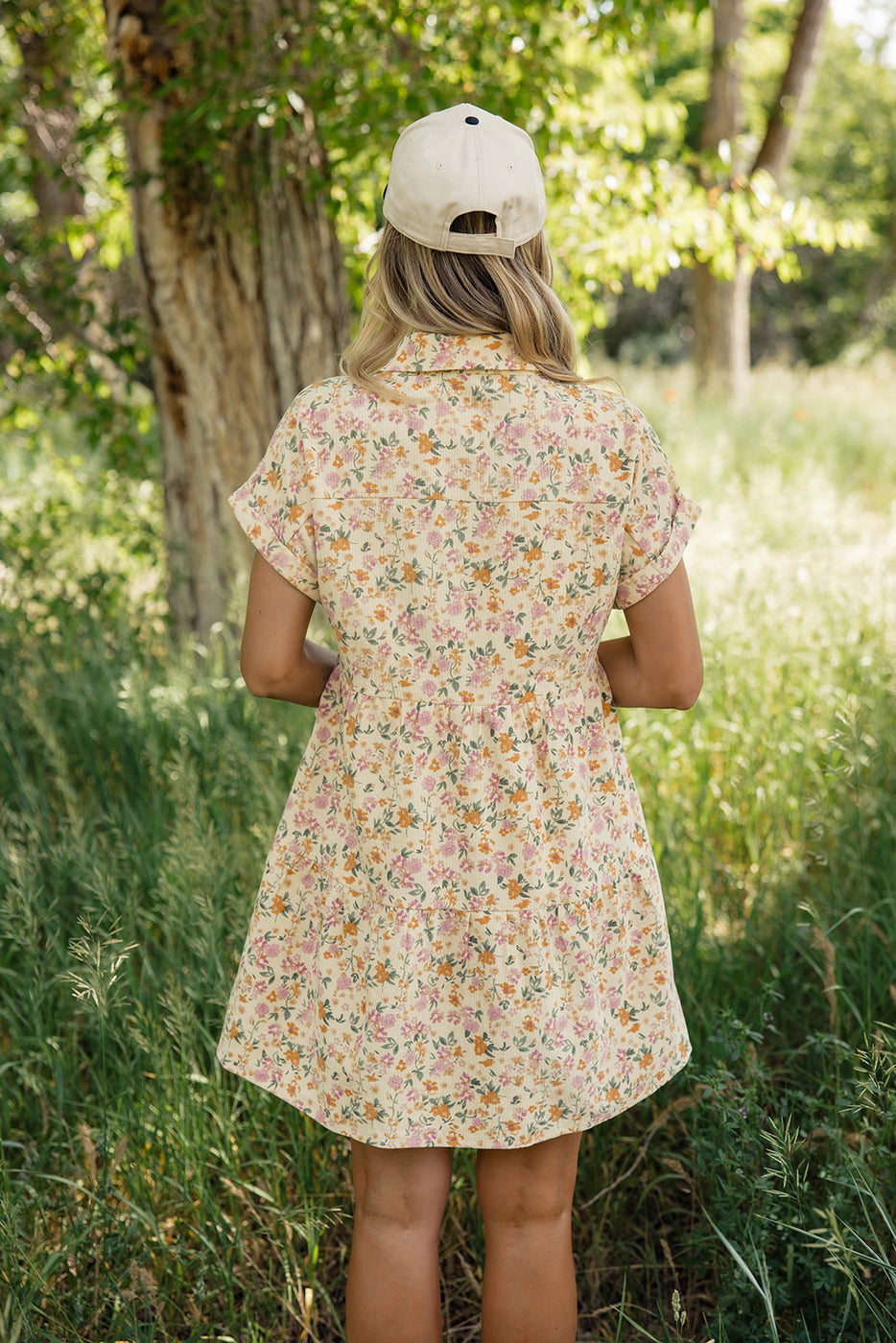 a woman in a dress and hat standing in tall grass