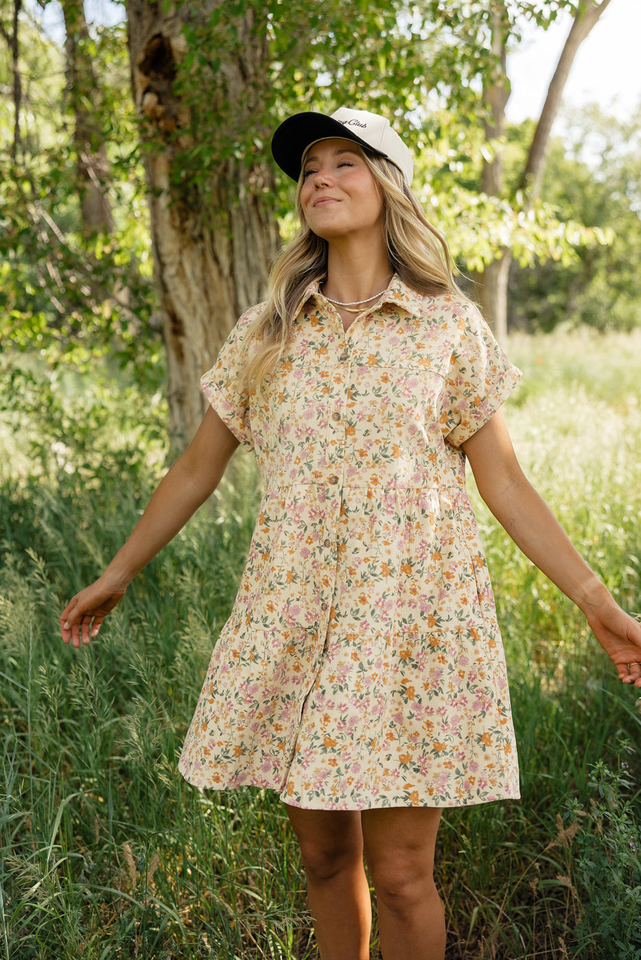 a woman in a dress and hat standing in a grassy area