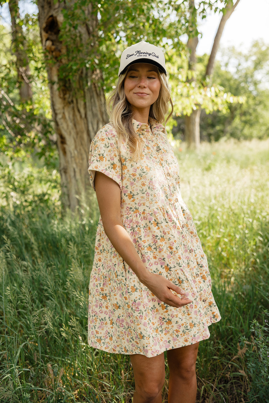 a woman in a dress and hat standing in a field of tall grass