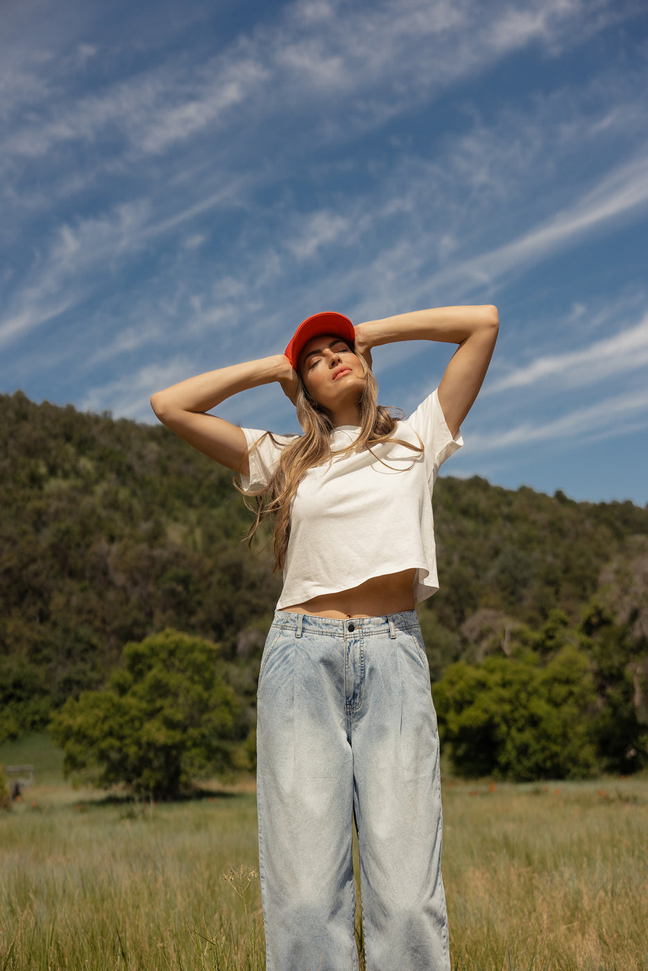 a woman in a white shirt and blue jeans with her hands on her head