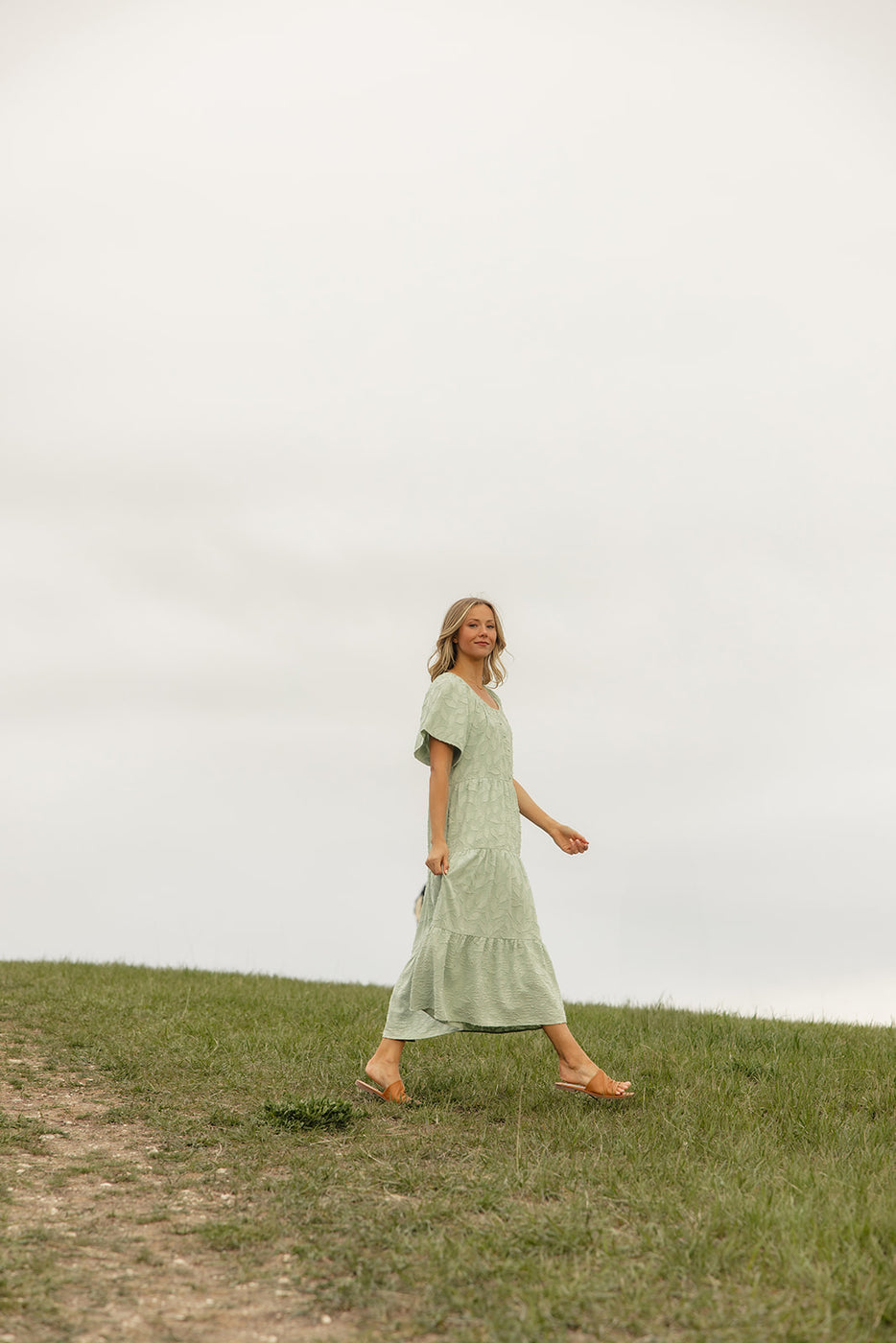 a woman in a dress walking on a grassy hill
