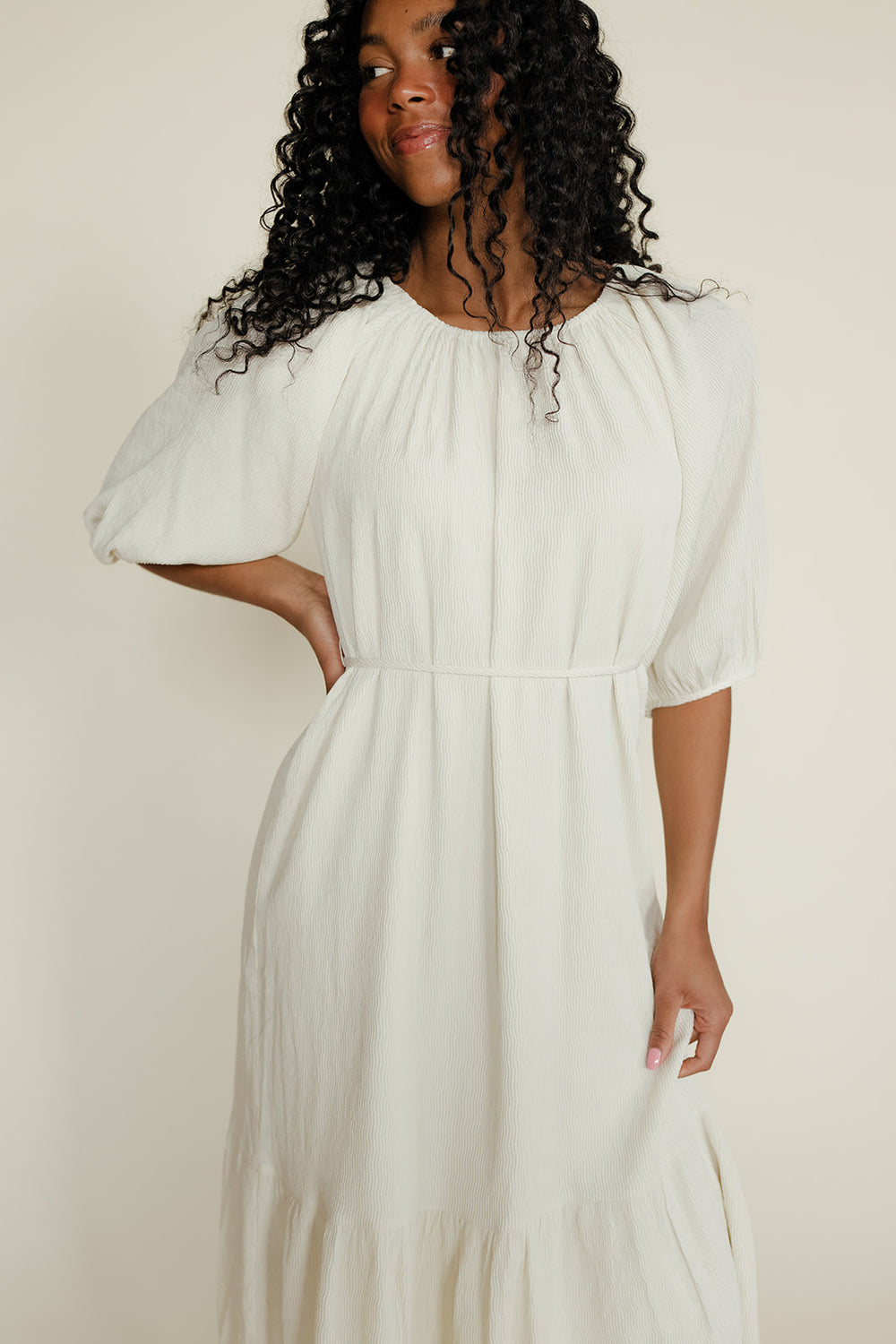 Woman wearing a white dress with puffed sleeves against a plain background