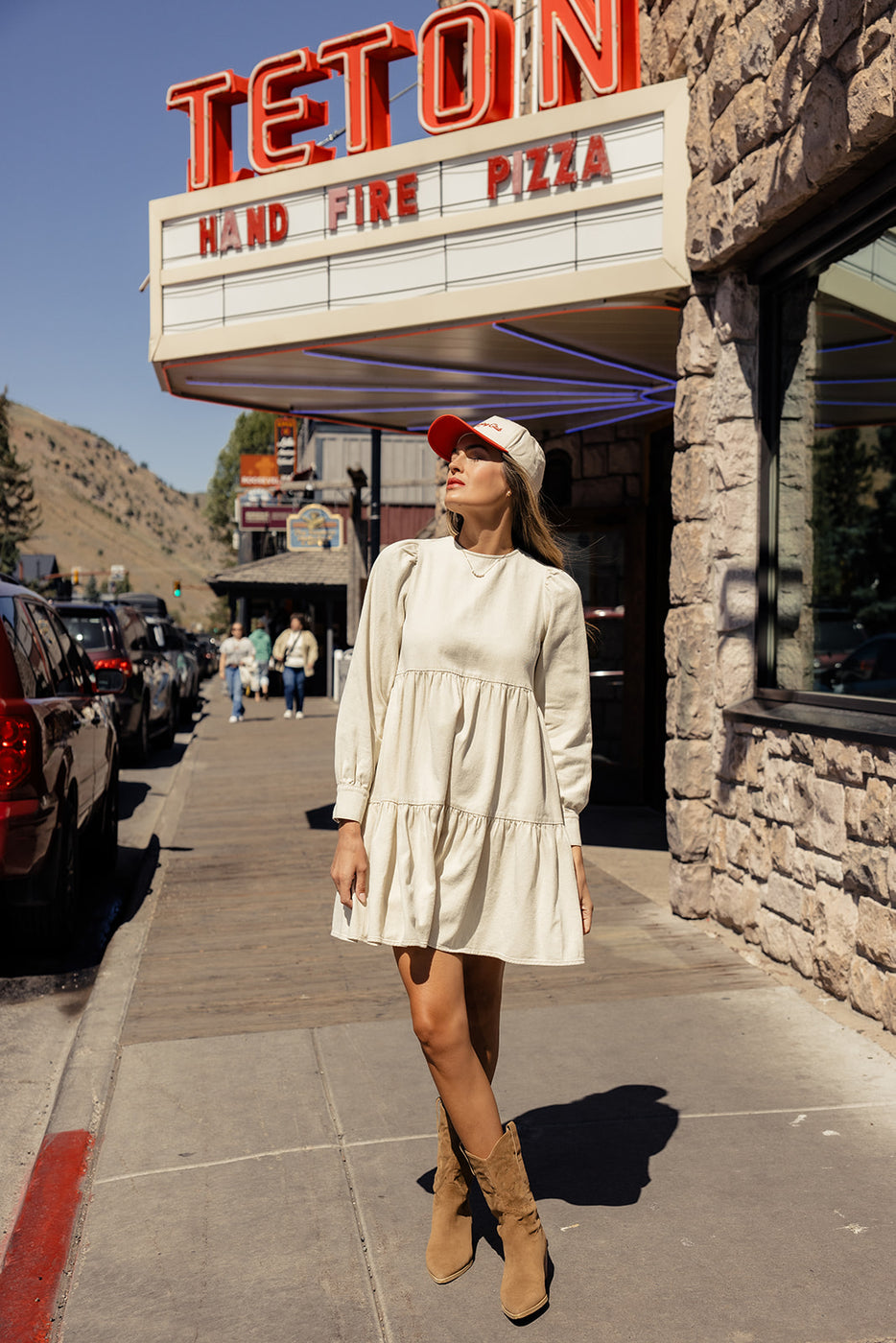 a woman in a white dress and a red hat standing on a sidewalk