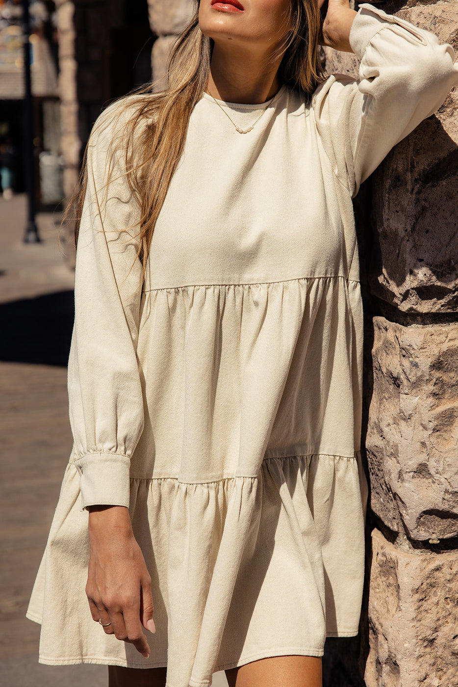 a woman in a white dress leaning against a stone wall