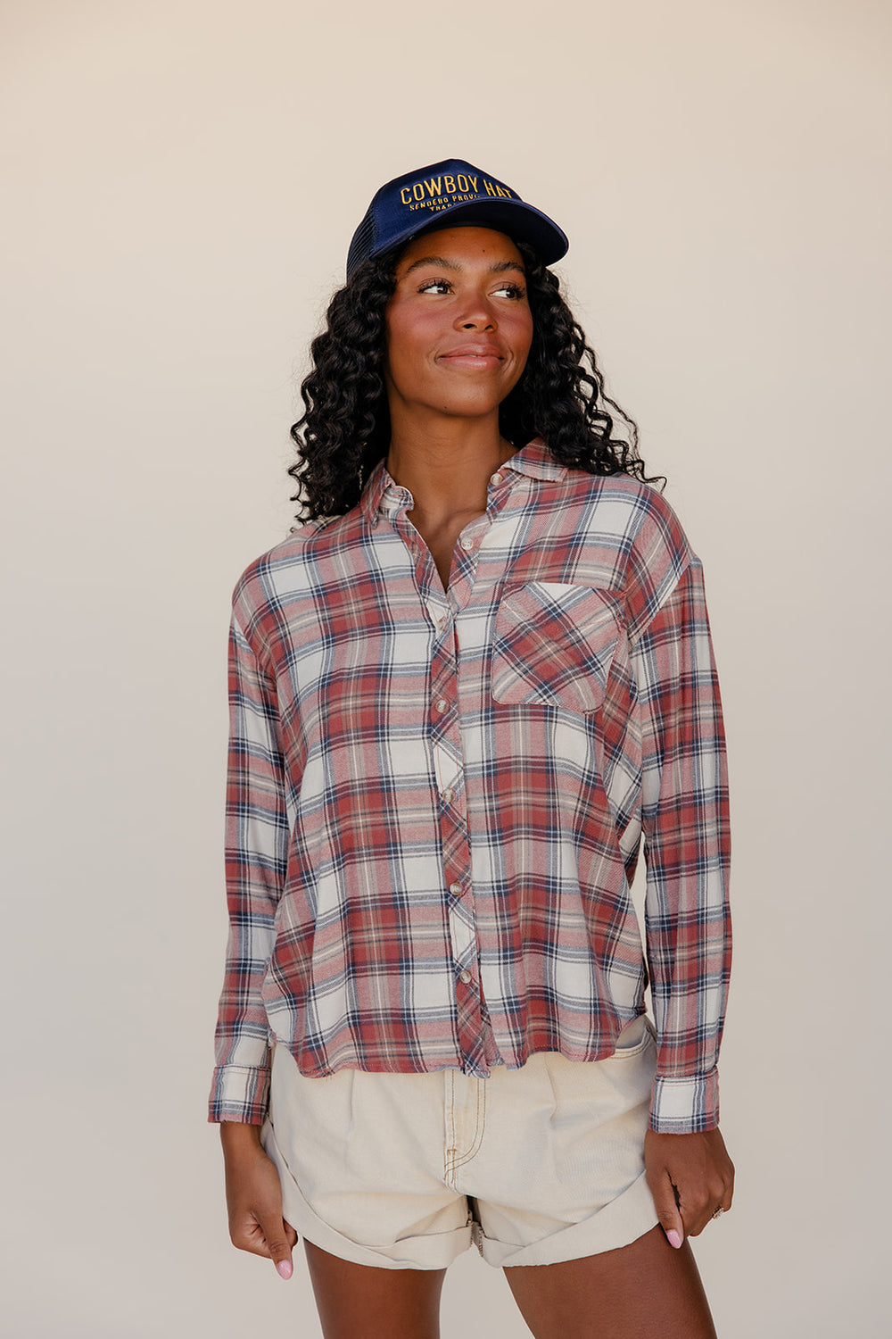 Woman wearing a plaid shirt and cap against a plain background