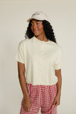 Woman wearing a white shirt and red checkered pants with a beige cap on a plain background