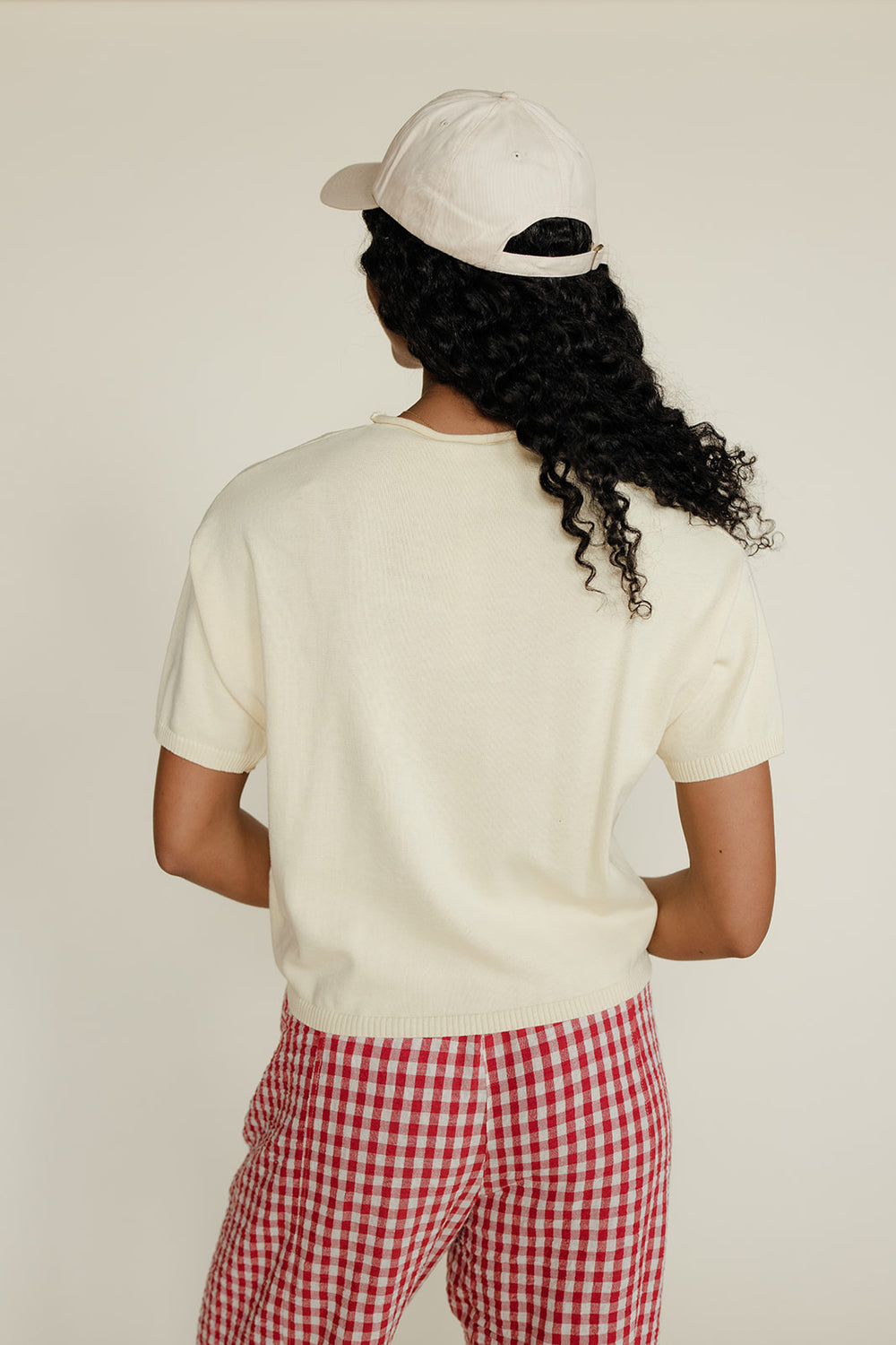Person wearing a white t-shirt and red checkered pants with a white cap on a plain background