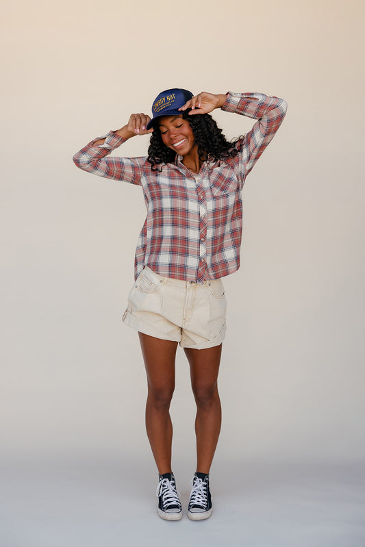 Person wearing a plaid shirt, shorts, and a cap on a plain background