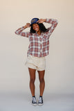 Person wearing a plaid shirt, shorts, and a cap on a plain background