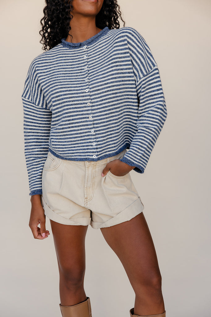 Person wearing a blue and white striped shirt and beige shorts against a plain background