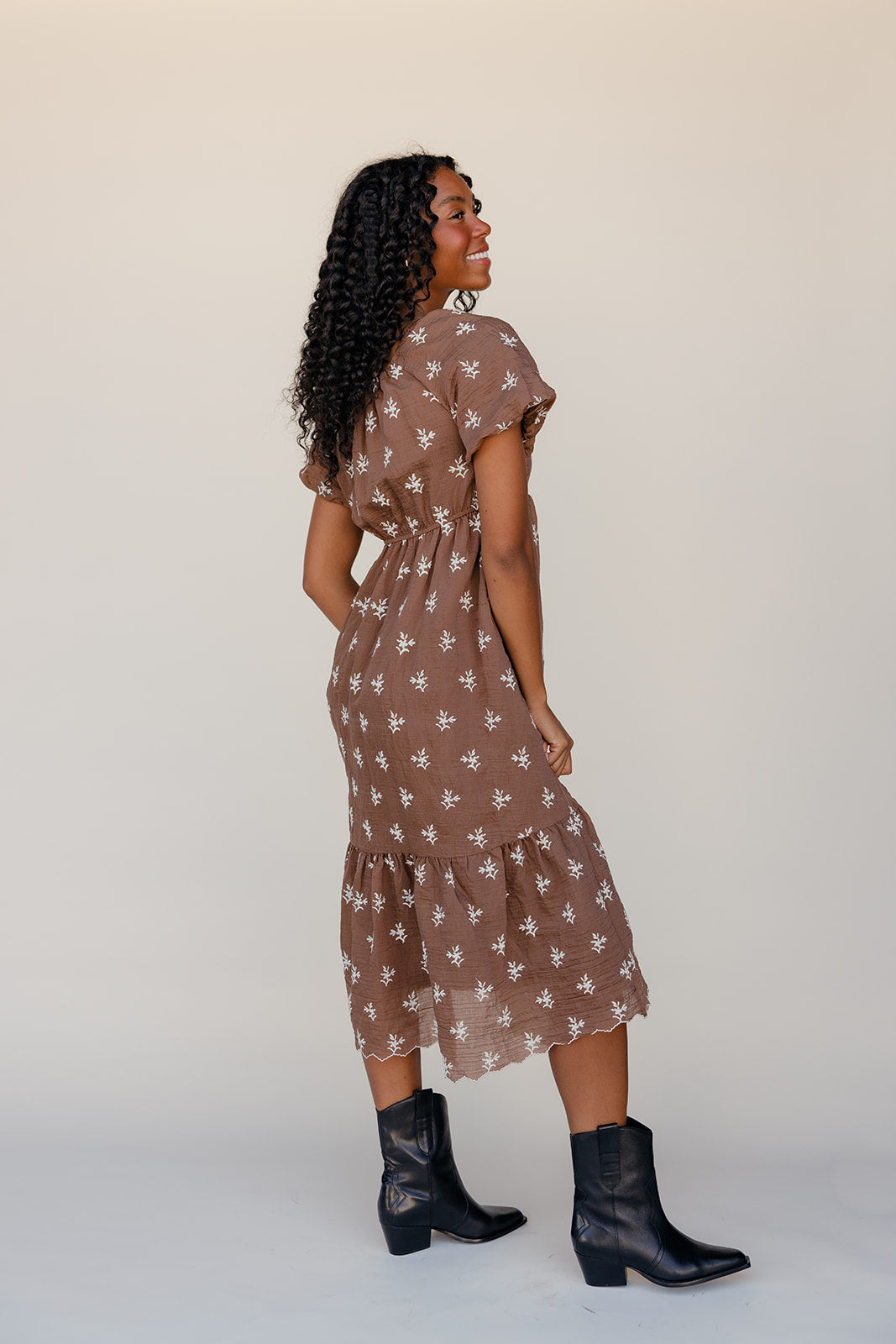 Woman wearing a brown floral dress with black boots on a white background