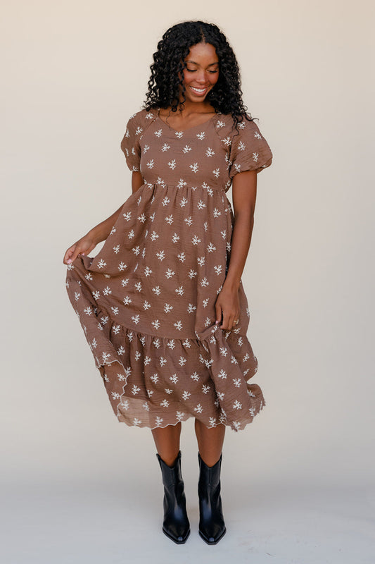 Woman wearing a brown floral dress with black boots on a white background