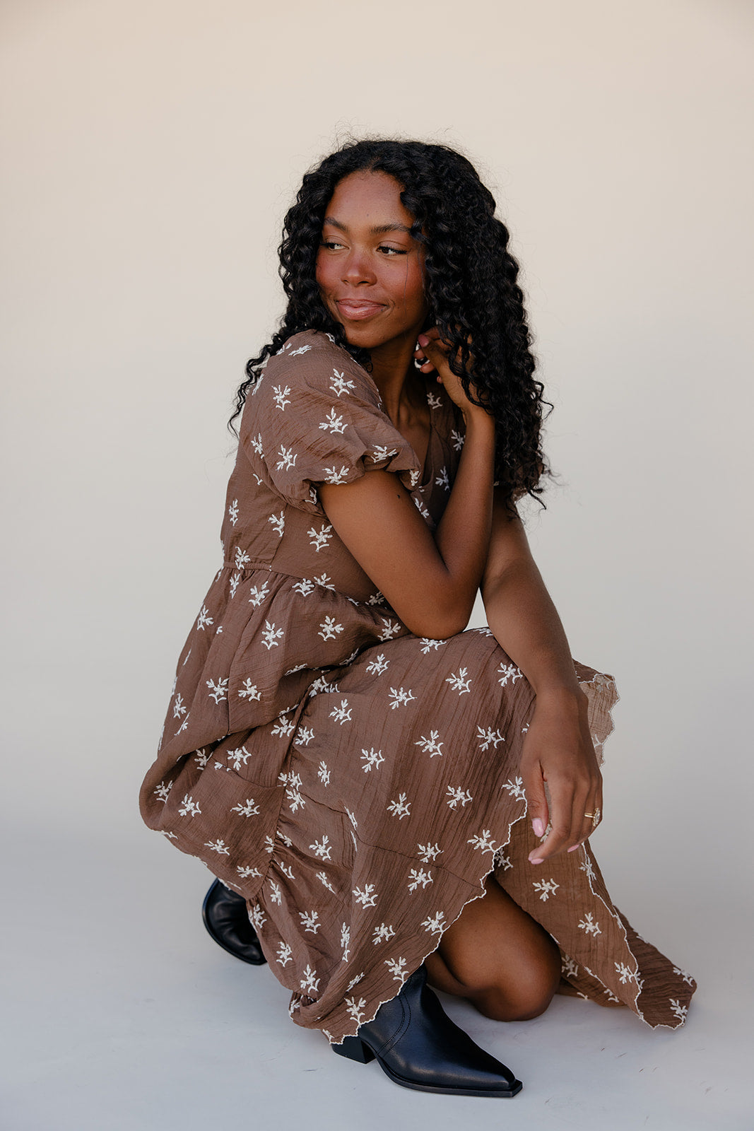 Woman in a brown floral dress posing against a white background