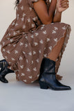 Person wearing a brown dress with white floral pattern and black boots on a light background