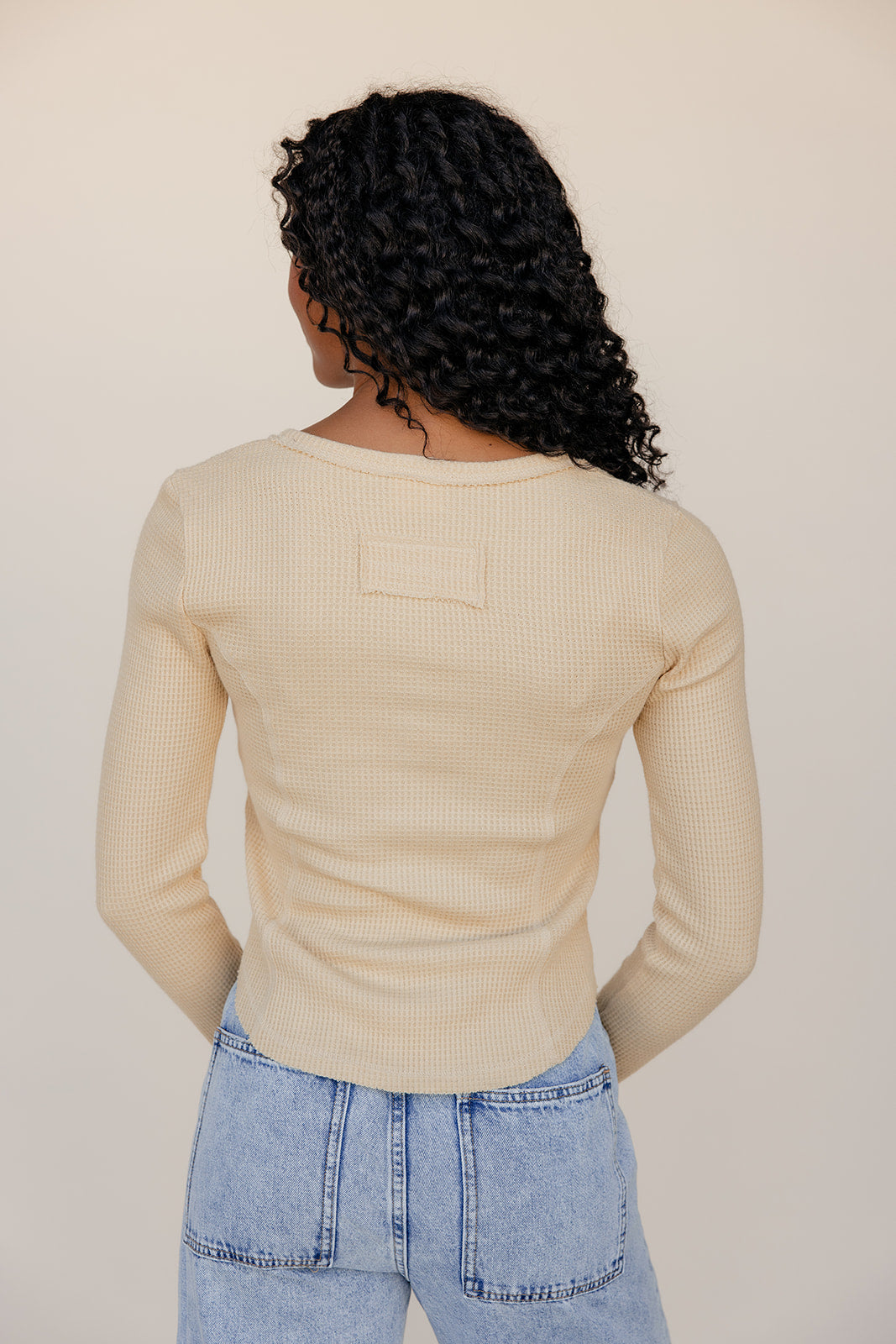 Person wearing a beige ribbed sweater and blue jeans against a plain background