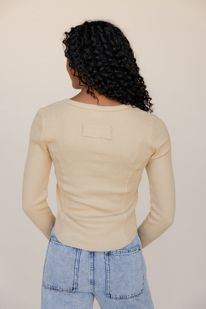 Person wearing a beige ribbed sweater and blue jeans against a plain background