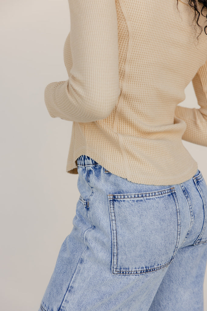 Person wearing a beige ribbed sweater and light blue jeans against a plain background