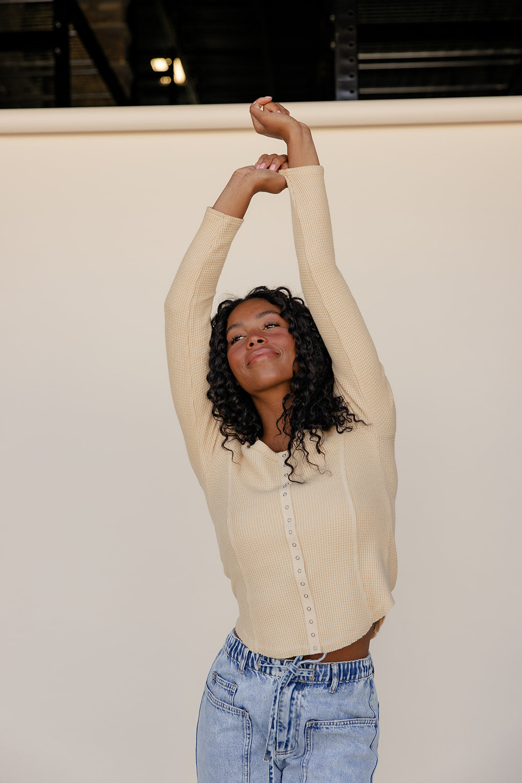 Woman stretching with arms above head against a plain background