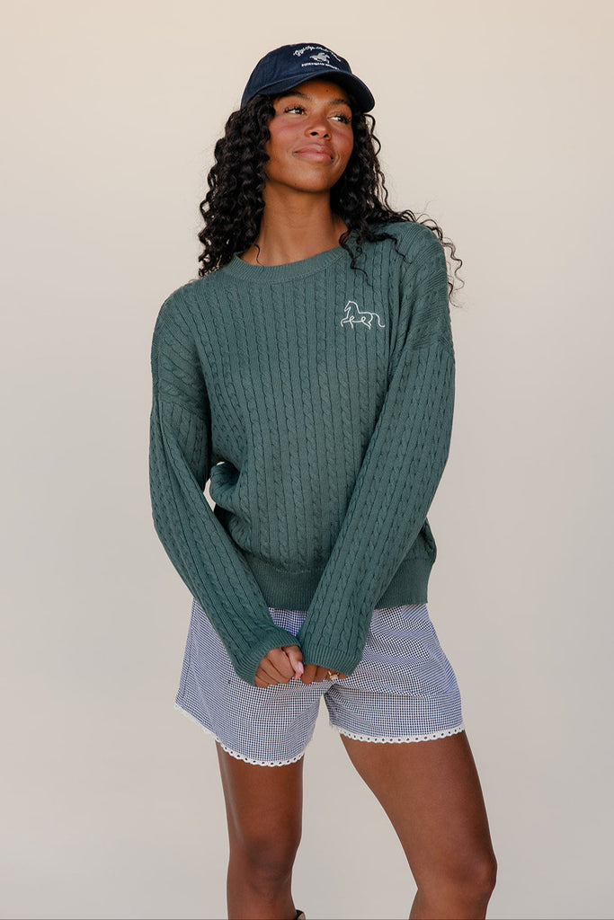 Woman wearing a green sweater and blue shorts with a white background