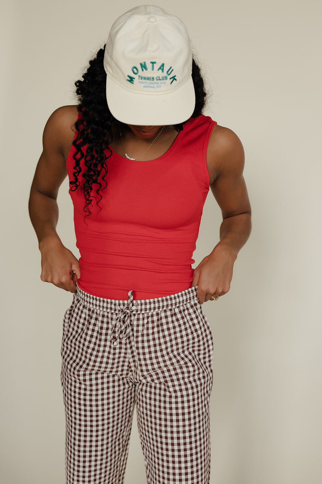 Person wearing a red tank top, checkered pants, and a white cap with 'Montana' text on a beige background