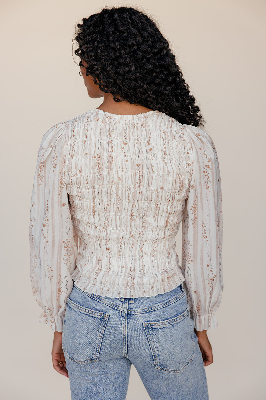 Person wearing a patterned blouse and jeans against a plain background