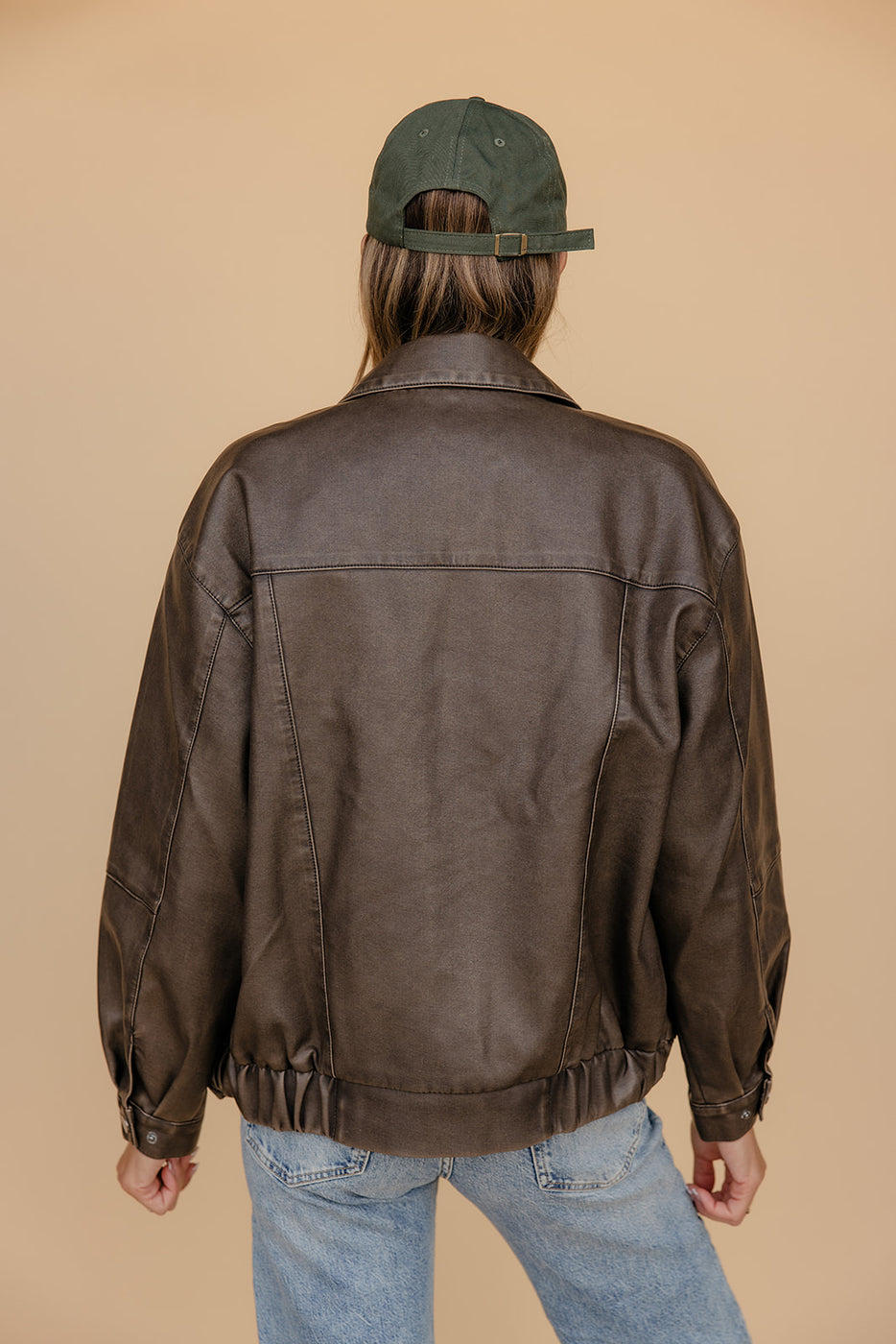 Person wearing a brown leather jacket and blue jeans against a beige background